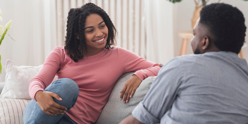 Married Black couple sitting on couch talking about finances 
