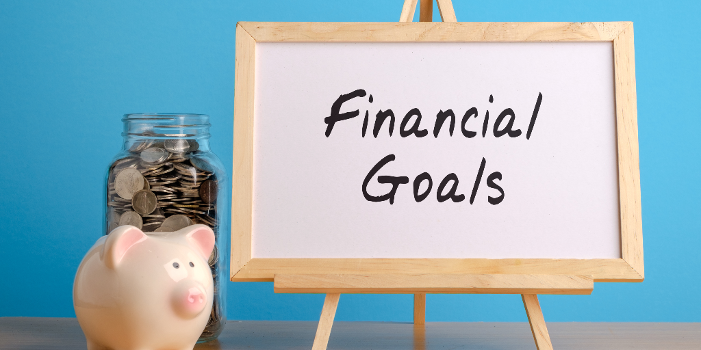 board with financial goals on it and a piggy bank with a glass jar filled with coins.